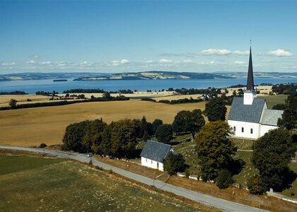 Stange kirke i det rike jordbrukslandskapet i Vestbygda med Hovinsholmen, Helgøya og Nes i bakgrunnen.  - Klikk for stort bilde