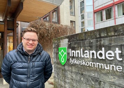Fylkesordfører Even Aleksander Hagen foran skilt med logoen til Innlandet fylkeskommune  - Klikk for stort bilde