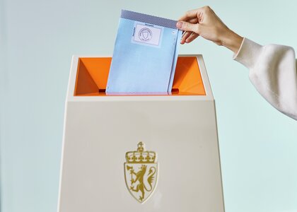 En blå stemmeseddel til fylkestingsvalget puttes ned i en valgurne - Klikk for stort bilde
